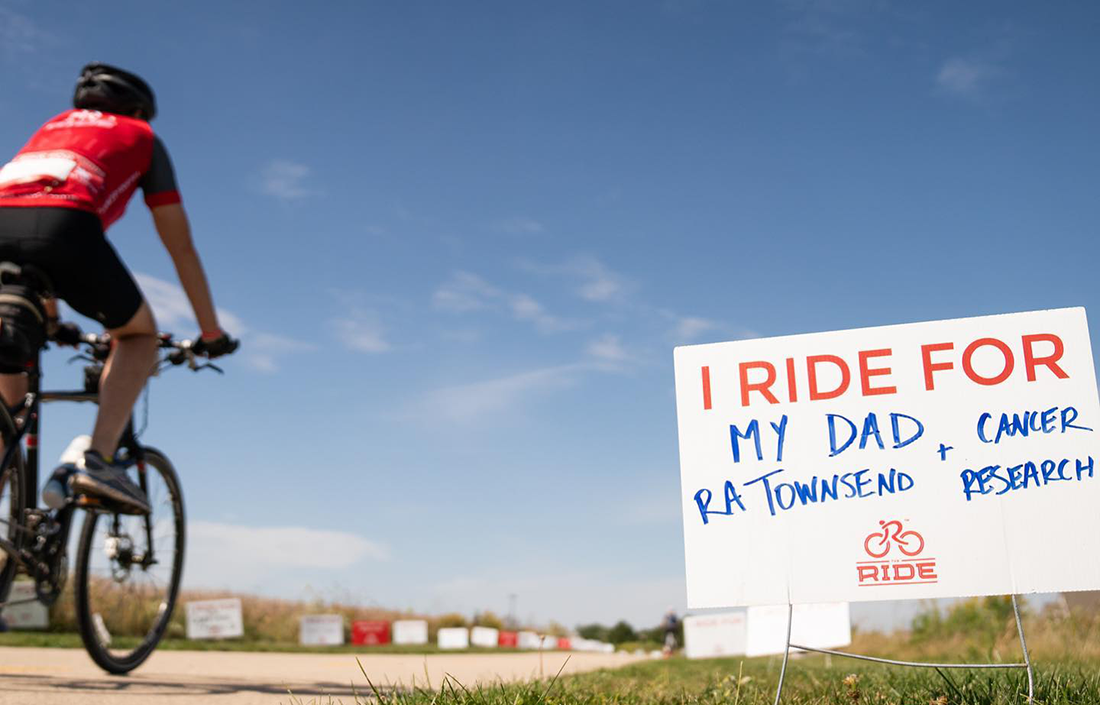 A bicyclist passes a yard sign dedicated to a cancer patient during 'The Ride' bike event.