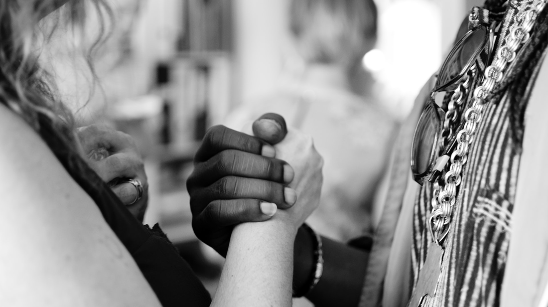 A white and a Black woman clasping hands.