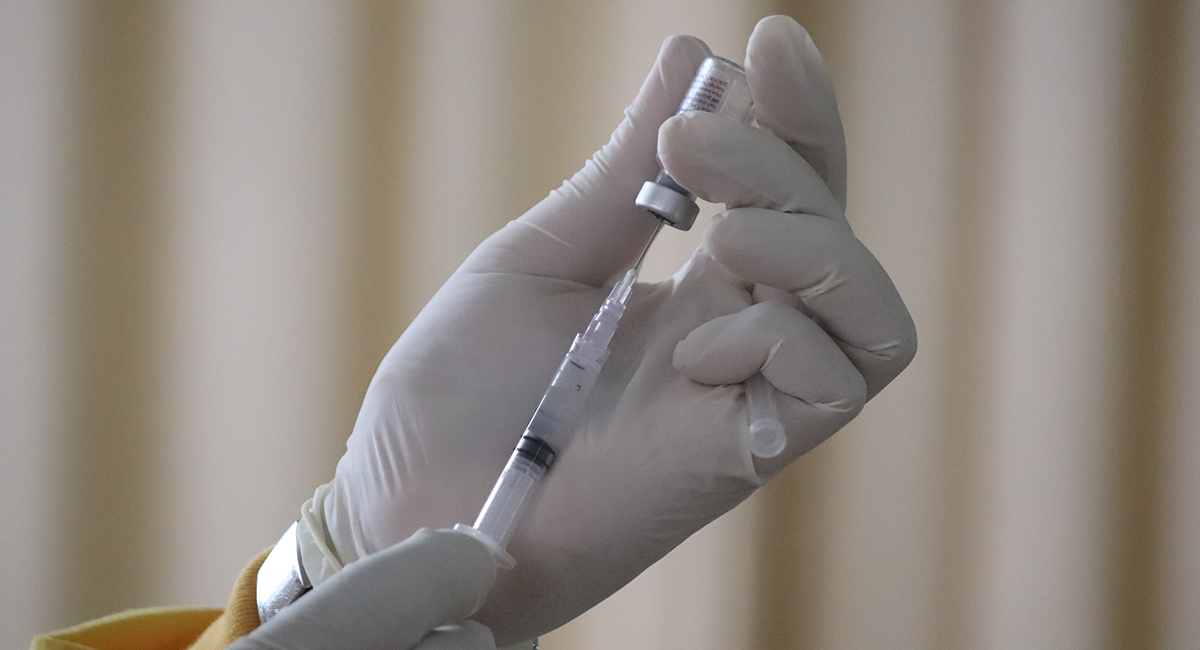 A researcher holds a vaccine vial and syringe.