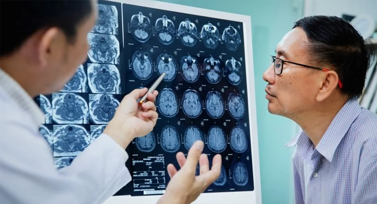 A physician speaks with a patient while looking at scans of a brain.