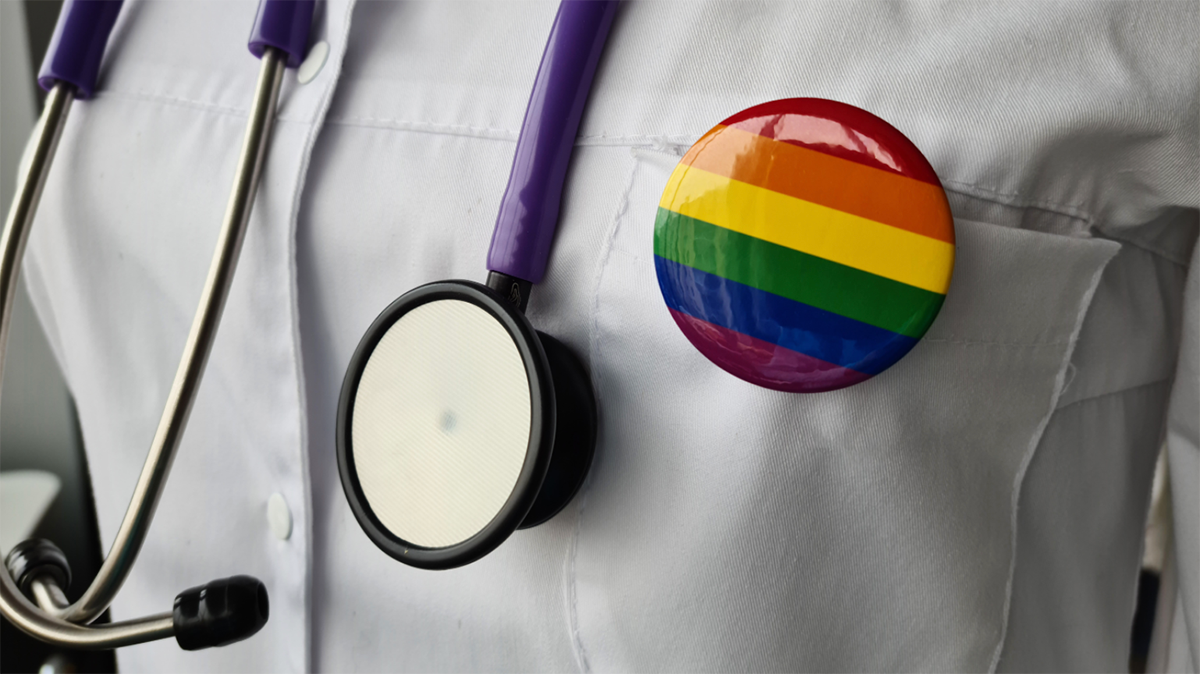 A physician with a stethoscope and a rainbow sticker on their chest.