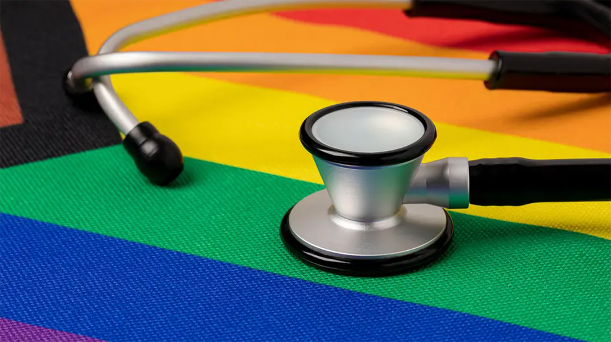 A black and white stethoscope lays on top of a rainbow-colored pride flag.